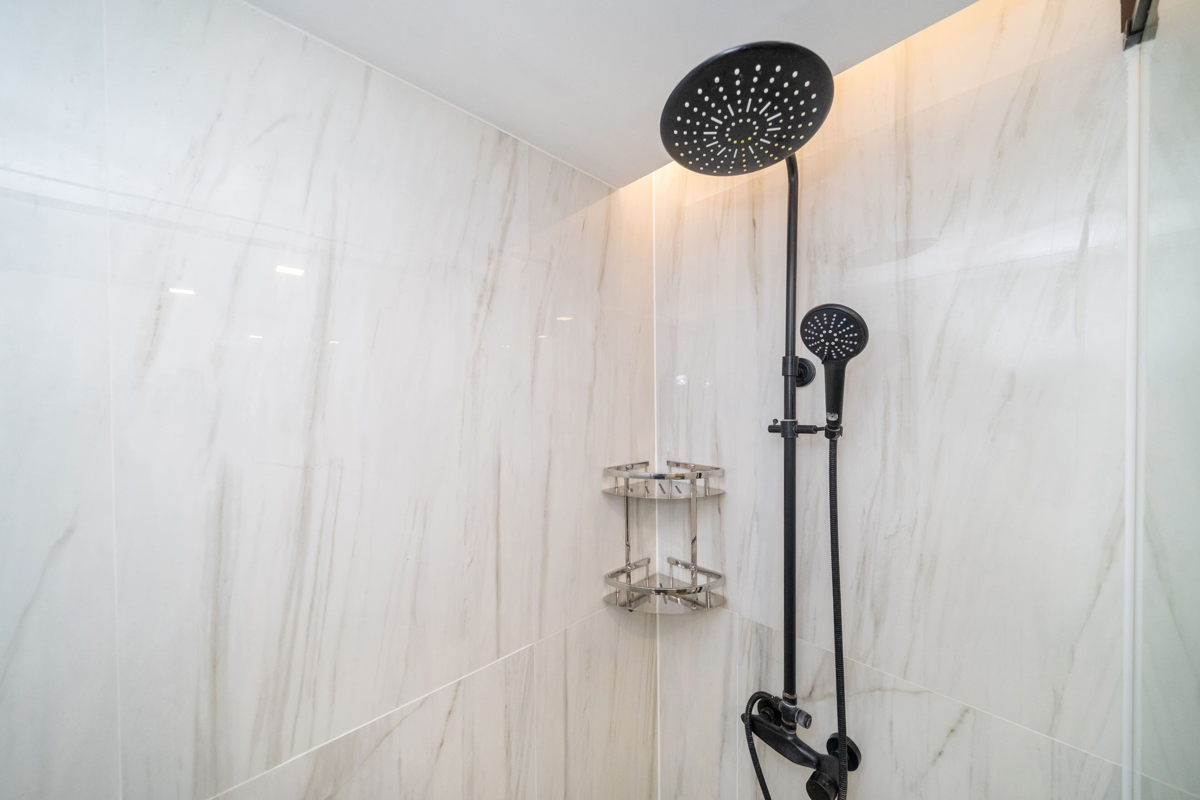 Een moderne badkamer met douche, glazen plank en marmeren wanden.