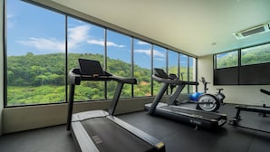 A gym with treadmills and exercise equipment, large windows with a view of a forested landscape. - Modern Studio Rooftop Pools UTKR 205 (Tambon Karon)