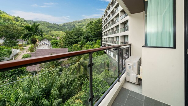 A modern hotel balcony with a glass railing overlooking a lush green landscape and a hillside. - Modern Studio Rooftop Pools UTKR 205 (Tambon Karon)