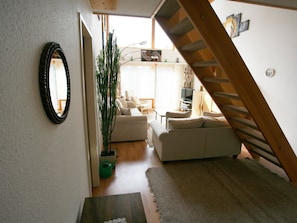 Un escalier menant à un espace de vie comprenant un canapé, une plante en pot et un miroir au mur.