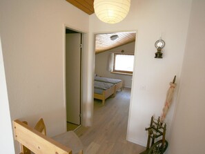 A narrow hallway leading to a bedroom with a sloped ceiling, a window with curtains, and a bed. - I dr Rehwiesa A32 Appartement/Fewo, Bad, WC, 2-Bettwohnung 2-Bettwohnung by Interhome (Arosa)