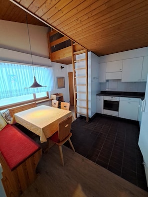 A compact kitchen with a dining area, wooden ceiling, and a window with blinds. - I dr Rehwiesa B31 Appartement/Fewo, Bad, WC, 4-Bettwohnung by Interhome (Arosa)