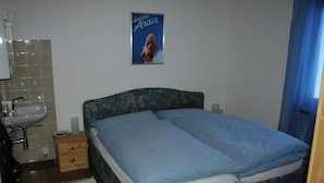 Ein Schlafzimmer mit einem Bett, einem Nachttisch, einem Wandposter und einem Badezimmer mit Waschbecken und Spiegel.