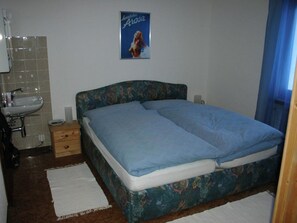 Ein Schlafzimmer mit einem Bett, einem Nachttisch, einem Wandposter und einem Badezimmer mit Waschbecken und Spiegel.