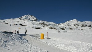 Ein verschneiter Berghang mit Skifahrern und einer gelben Absperrung.