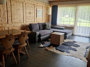 Ein gemütliches Zimmer mit Holztisch, Stühlen, einer Couch und einem Teppich.