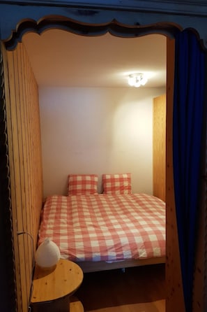 Ein kleines, gemütliches Zimmer mit einer karierten Bettdecke, einer Nachttischlampe und einem hölzernen Kopfteil.