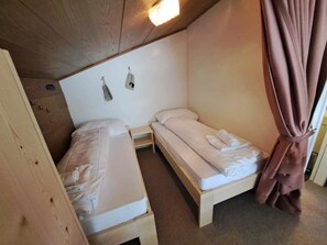 A small, compact room with two single beds, a wooden ceiling, and a light fixture. - I dr Rehwiesa C21 Appartement/Fewo, Bad, WC, 4-Bettwohnung 4-Bettwohnung by Interhome (Arosa)