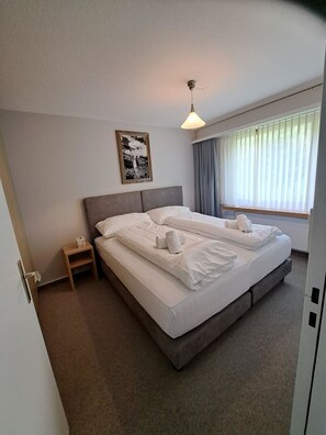 Een hotelkamer met een groot bed, nachtkastje, wanddecoratie en een raam met gordijnen.