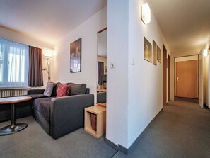 A hotel room with a sofa, a small table, a lamp, a painting, and a hallway leading to a door. - Paradies 110 Appartement/Fewo, Dusche, WC, 4-Bettwohnung 4-Bettwohnung by Interhome (Arosa)