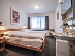 Una camera d'albergo con un letto, una sedia, una scrivania, un lavandino e una finestra con tende.