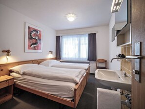 A hotel room with a double bed, a bedside table, a chair, a window with curtains, a bathroom with a sink and mirror, and a painting on the wall. - Paradies 110 Appartement/Fewo, Dusche, WC, 4-Bettwohnung 4-Bettwohnung by Interhome (Arosa)