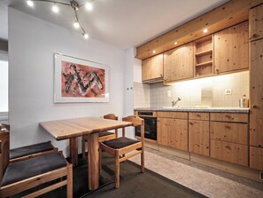 A modern kitchen with wooden cabinets, a dining table with chairs, and a painting on the wall. - Paradies 110 Appartement/Fewo, Dusche, WC, 4-Bettwohnung 4-Bettwohnung by Interhome (Arosa)