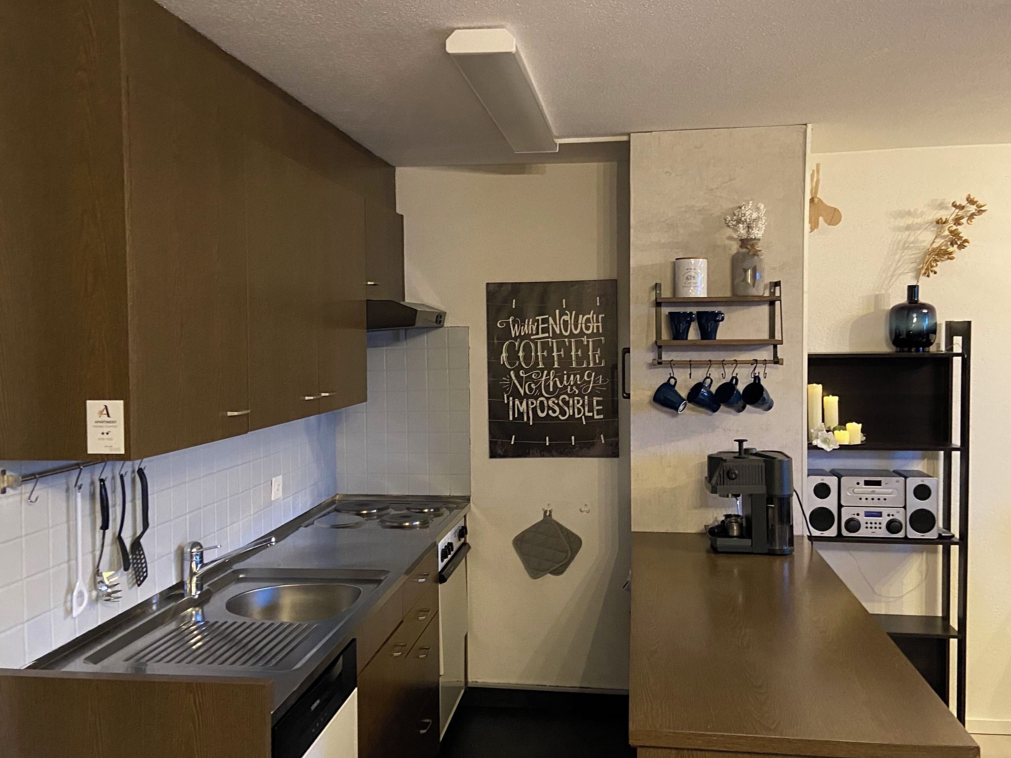 Eine Küche mit Herd, Spüle und Schränken. An der Wand hängt eine Schiefertafel mit einem Kaffee-Zitat.