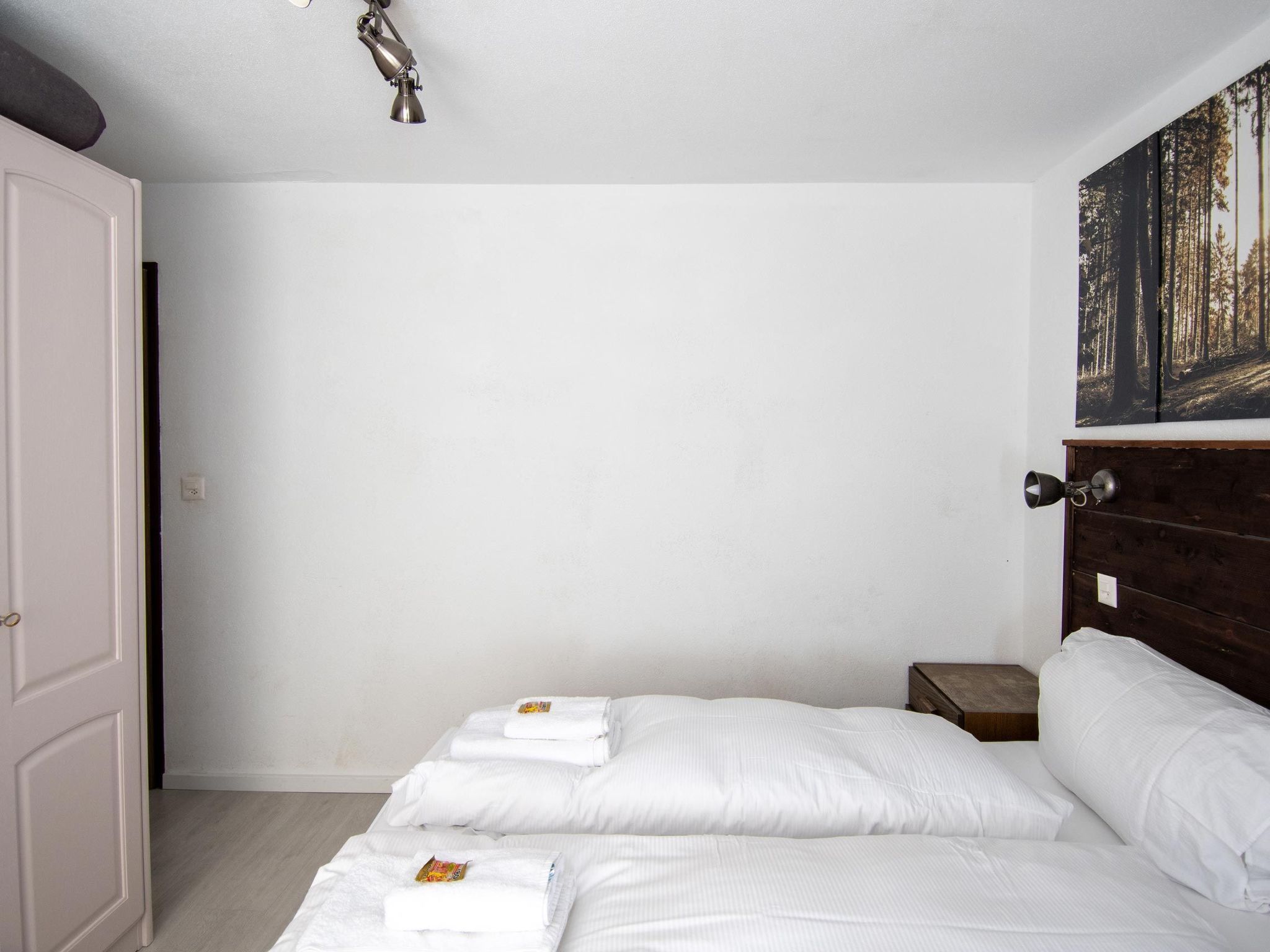 Un dormitorio con cama, mesita de noche, una puerta y una lámpara de pared.
