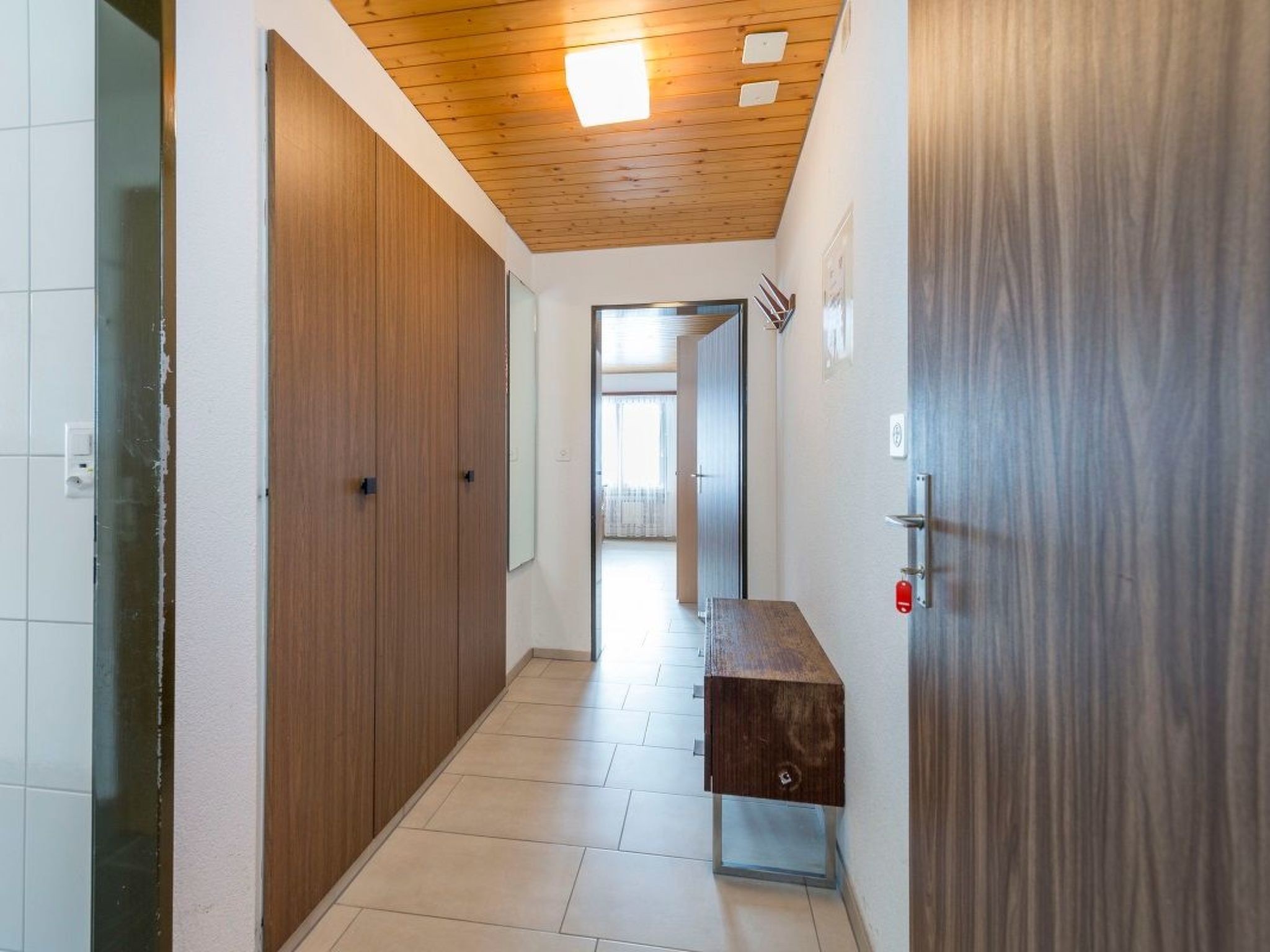 A hallway with wooden doors, a bench, and a ceiling light.