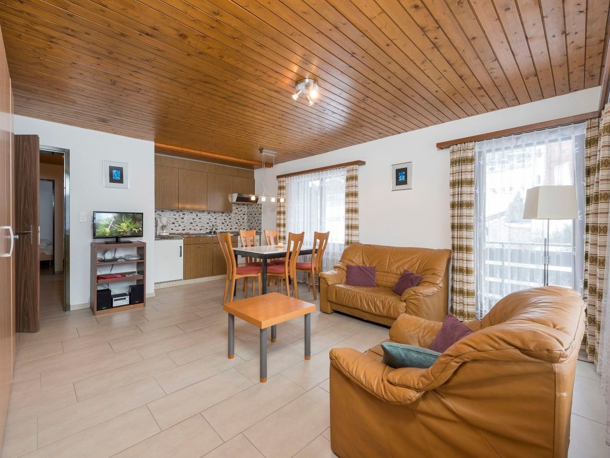 A modern living room with a brown leather sofa, a wooden dining table with chairs, and a kitchen in the background.