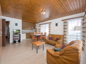 A modern living room with a brown leather sofa, a wooden dining table with chairs, and a kitchen in the background. - Valaisia 10, (Grächen), 1304 by Interhome (Grächen)