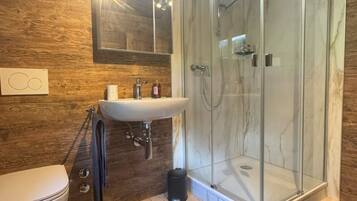 Ein Badezimmer mit Holzwand, einer Duschkabine aus Glas, einem weißen Waschbecken und einer Toilette.