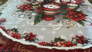 En julpyntad borddekoration med en festlig duk, en stor pepparkaksgubbe och ett julgran i bakgrunden.