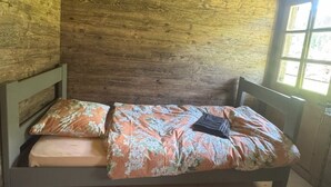 En säng för en person med ett blommigt överkast i ett rum med träväggar och ett sluttande tak.