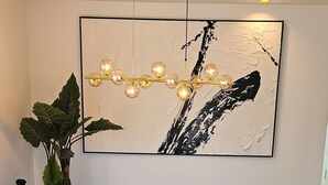 Et spiseområde med et marmorbord, to stole med blåt betræk, et guld- og blå-hexagonal design, et sort-hvidt abstrakt maleri og en hængende lysarmatur.