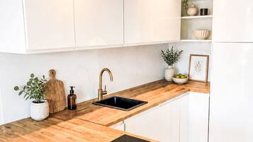 A modern kitchen with white cabinets, a wooden countertop, a black sink, and a stainless steel dishwasher.