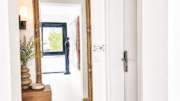 A hallway with a large mirror, a door, and a small table with a vase and a bowl.