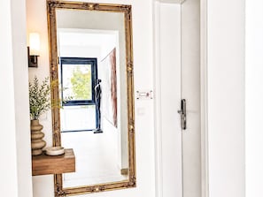 A hallway with a large mirror, a door, and a small table with a vase and a bowl. - mit Infinity-Pool by Interhome (Munich)