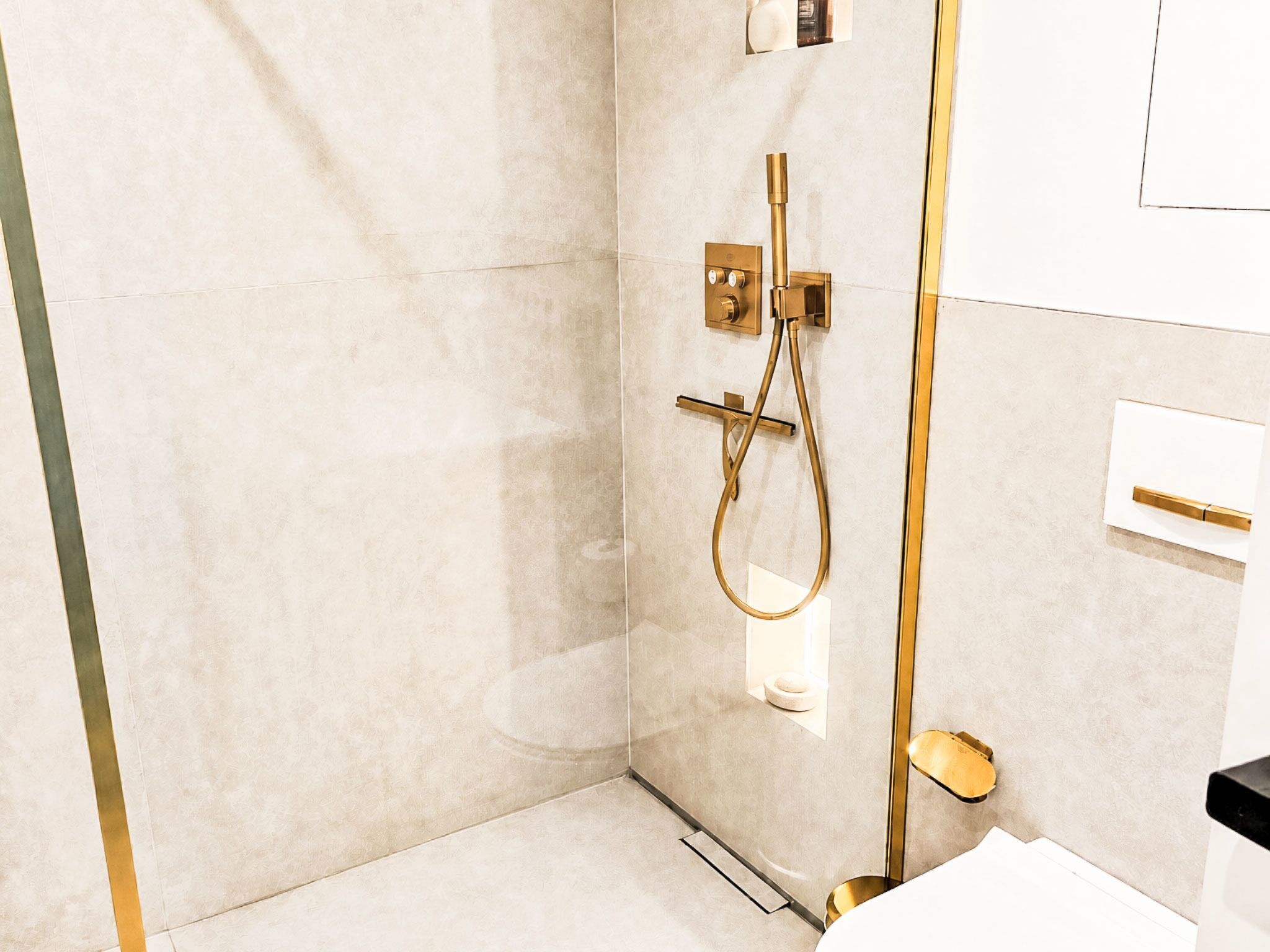 A modern bathroom with a glass shower enclosure, a gold showerhead, and a white sink.