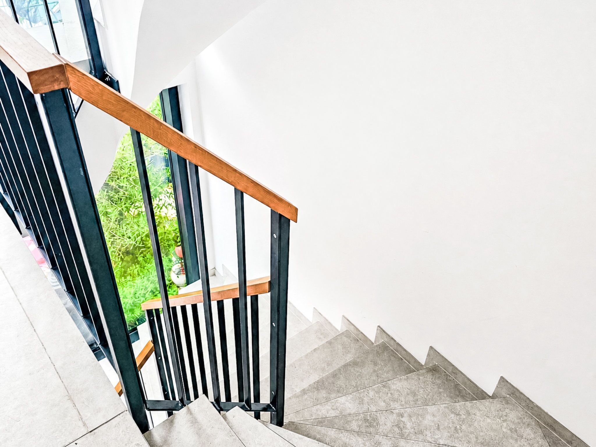 Eine Treppe mit hölzernem Geländer und schwarzen Spindeln, die zu einer Aussichtsplattform mit Blick auf Grünfläche führt.