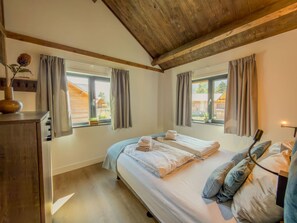 Ein Schlafzimmer mit einem Bett, zwei Fenstern, einer Holzbalkendecke und einer Nachttischlampe.