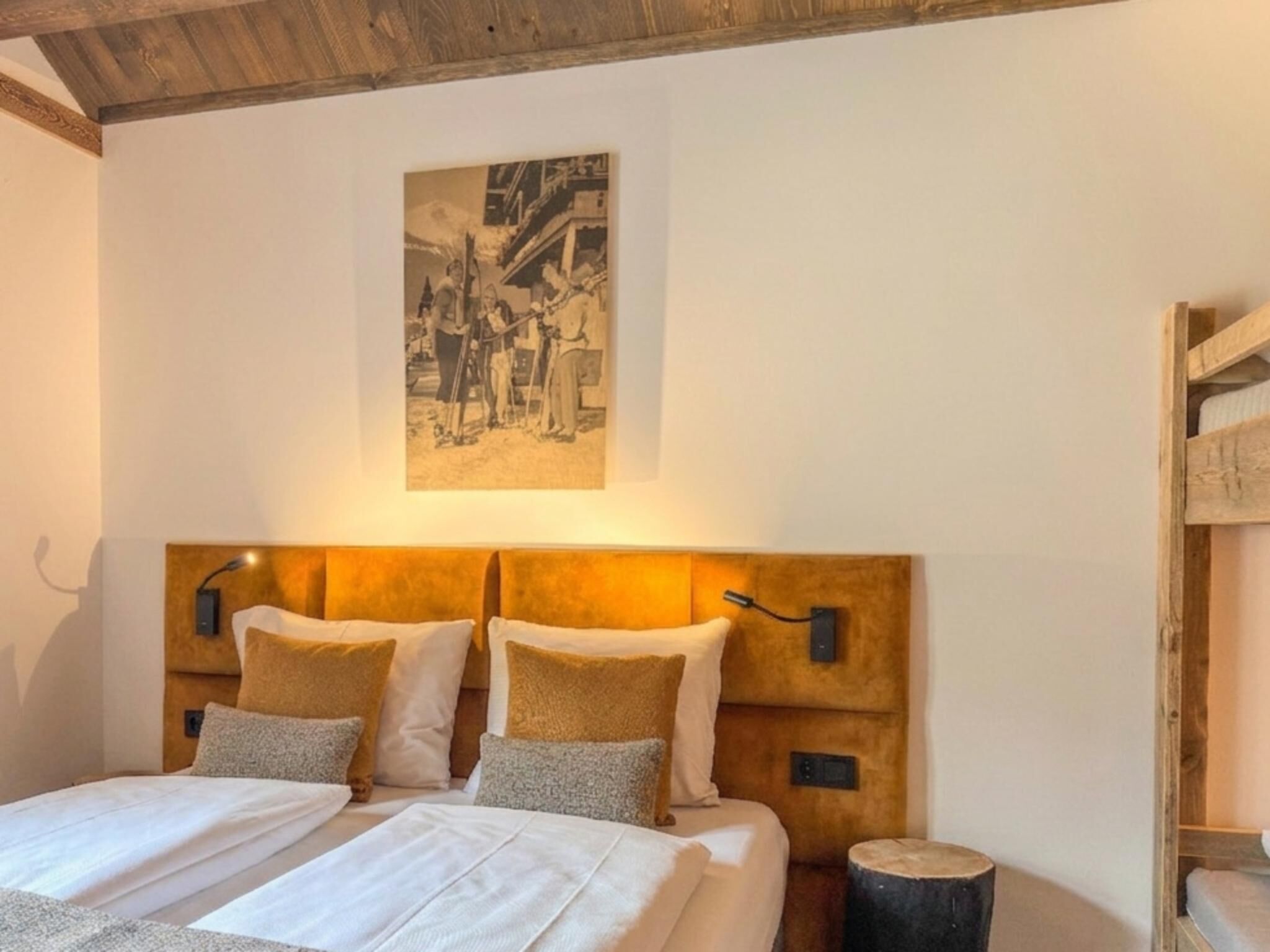 A bedroom with a bed, pillows, a headboard, a wall-mounted picture, and a bedside table.