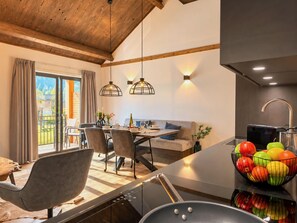Et moderne køkken med en central ø, spiseområde med stole og bord, samt udsigt til en balkon.