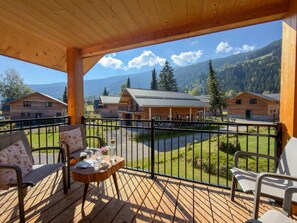 Une terrasse en bois avec une table et des chaises, offrant une vue sur un paysage montagneux parsemé de plusieurs bâtiments en bois.