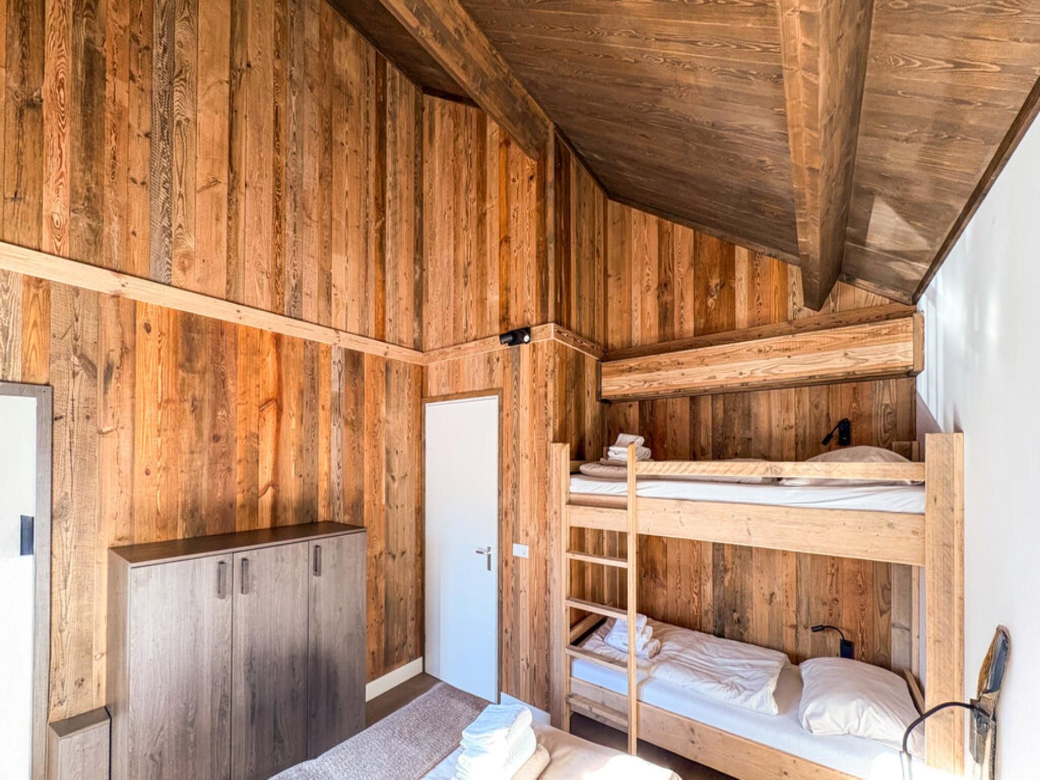 A wooden interior with bunk beds, a wardrobe, and a door.