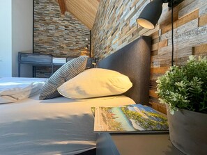 A modern bedroom with a bed, pillows, a bedside table, a lamp, and a wall with a wooden texture.