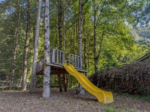 Un parque infantil con un tobogán amarillo en un área boscosa.