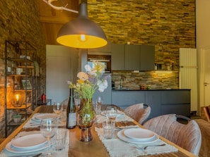 A dining area with a wooden table set for a meal, a vase with flowers, and a kitchen in the background. - Spacious holiday apartment by a lake in the Alps (Hermagor-Pressegger See)