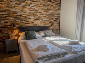Una cama bien hecha con sábanas y toallas blancas, cabecera y pared con diseño de tablones de madera.