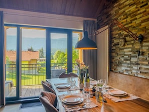 A dining area with a table set for two, a view of the outdoors, and a wooden wall with a clock. - Spacious holiday apartment by a lake in the Alps (Hermagor-Pressegger See)