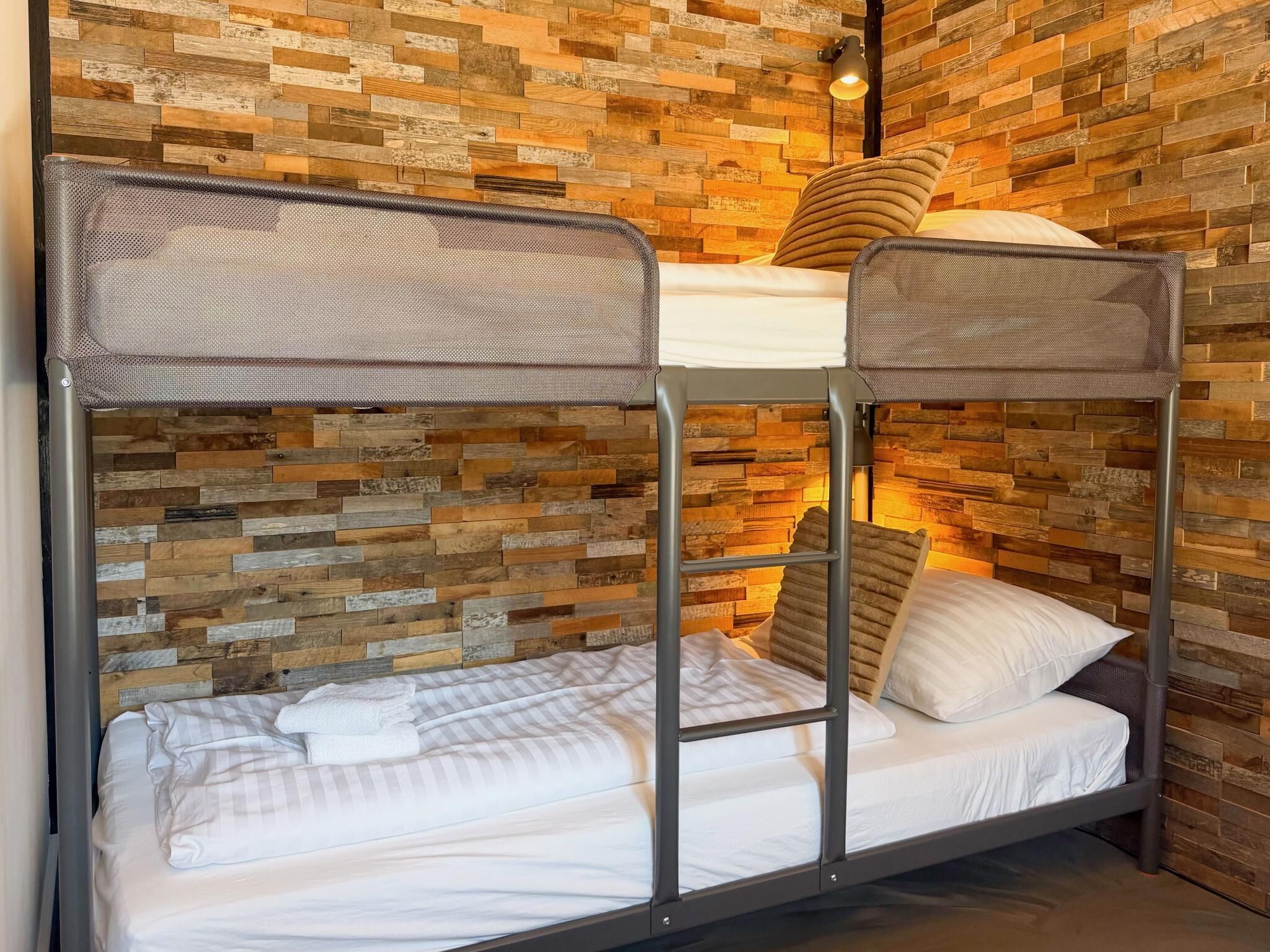 A bunk bed with a metal frame and a woven headboard, set against a wall with a wooden plank pattern.
