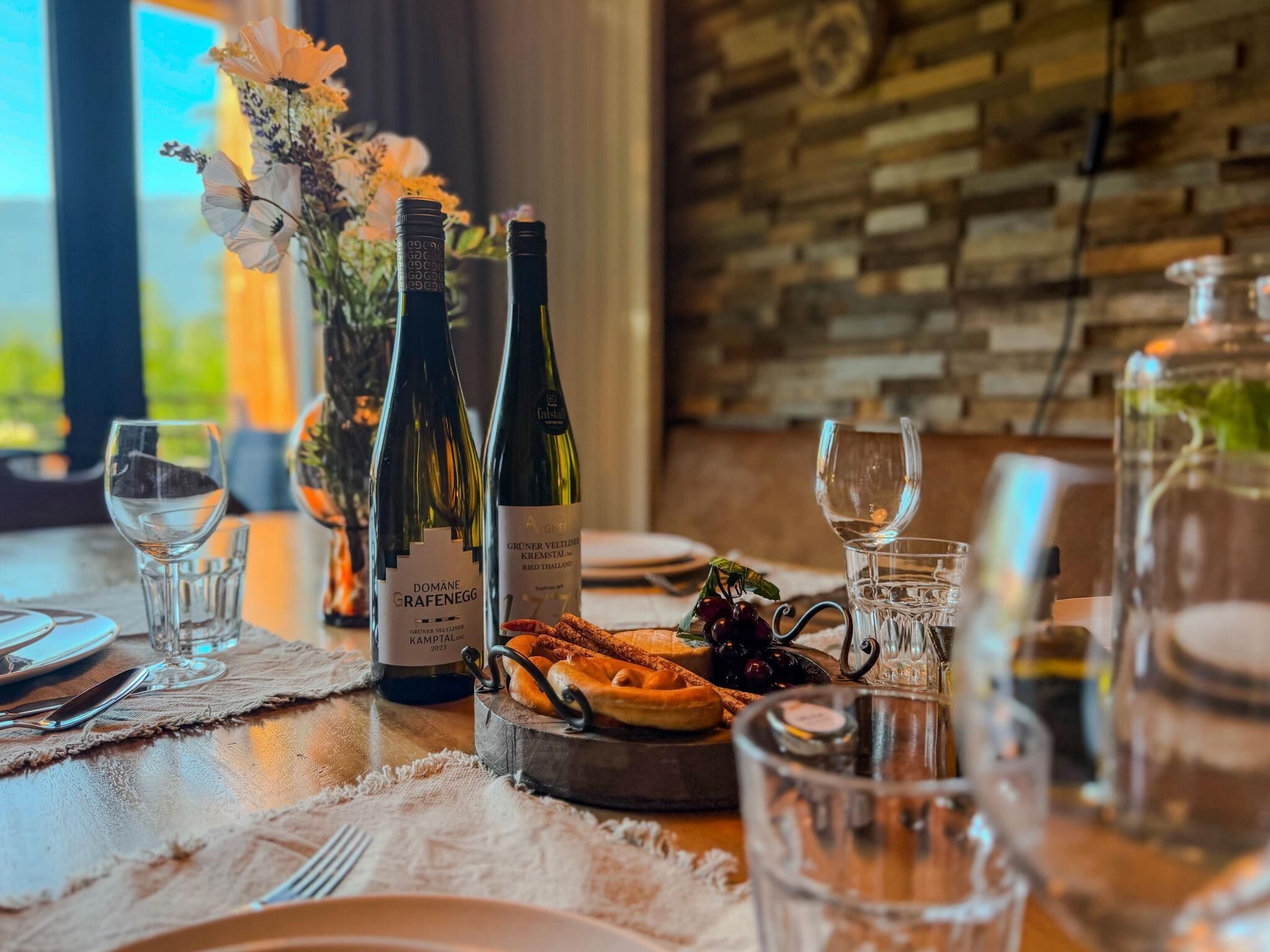 Uma mesa de jantar posta com garrafas de vinho, copos e um prato de comida.