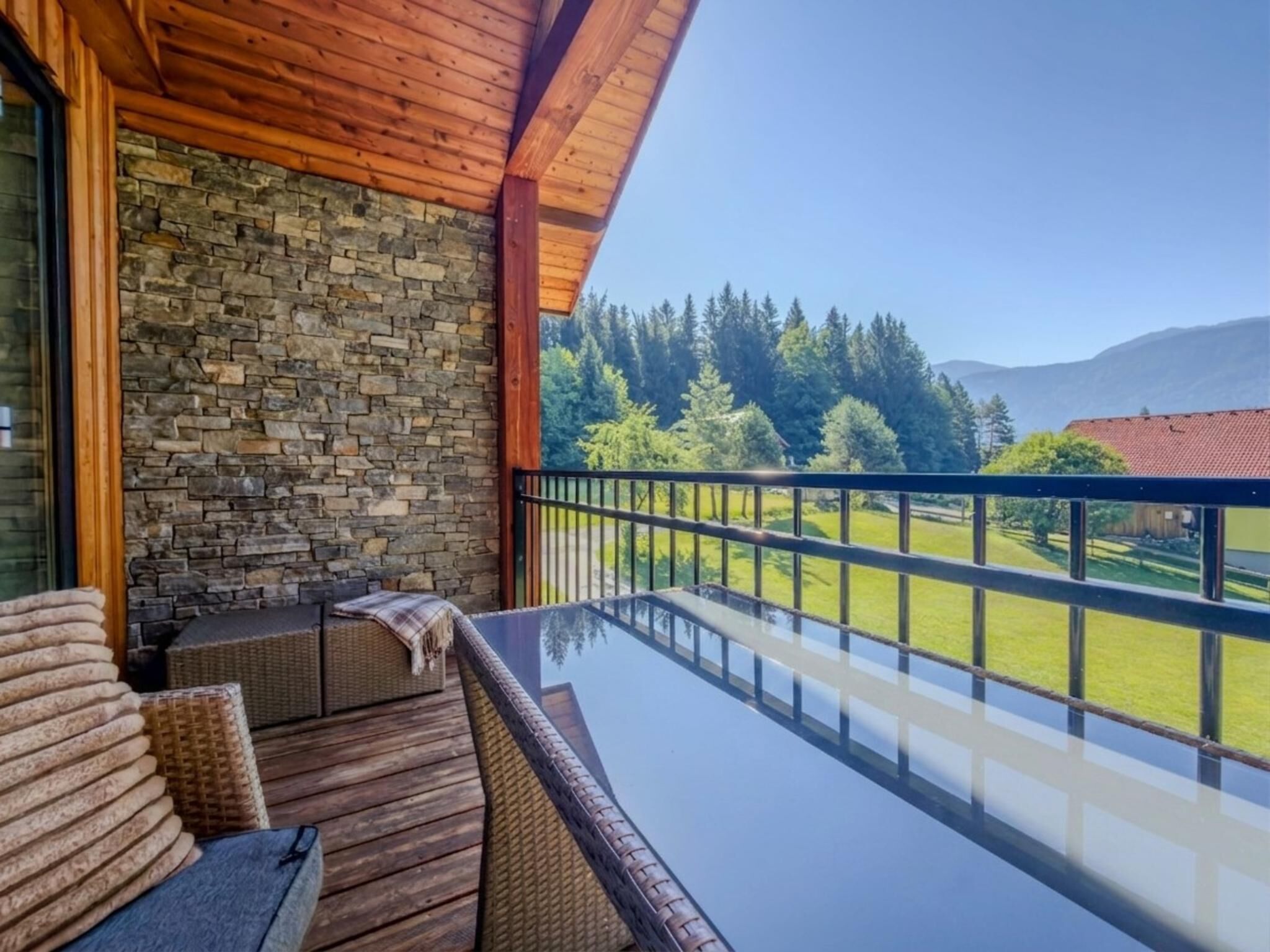 A balcony with a stone wall, wicker furniture, and a glass table.