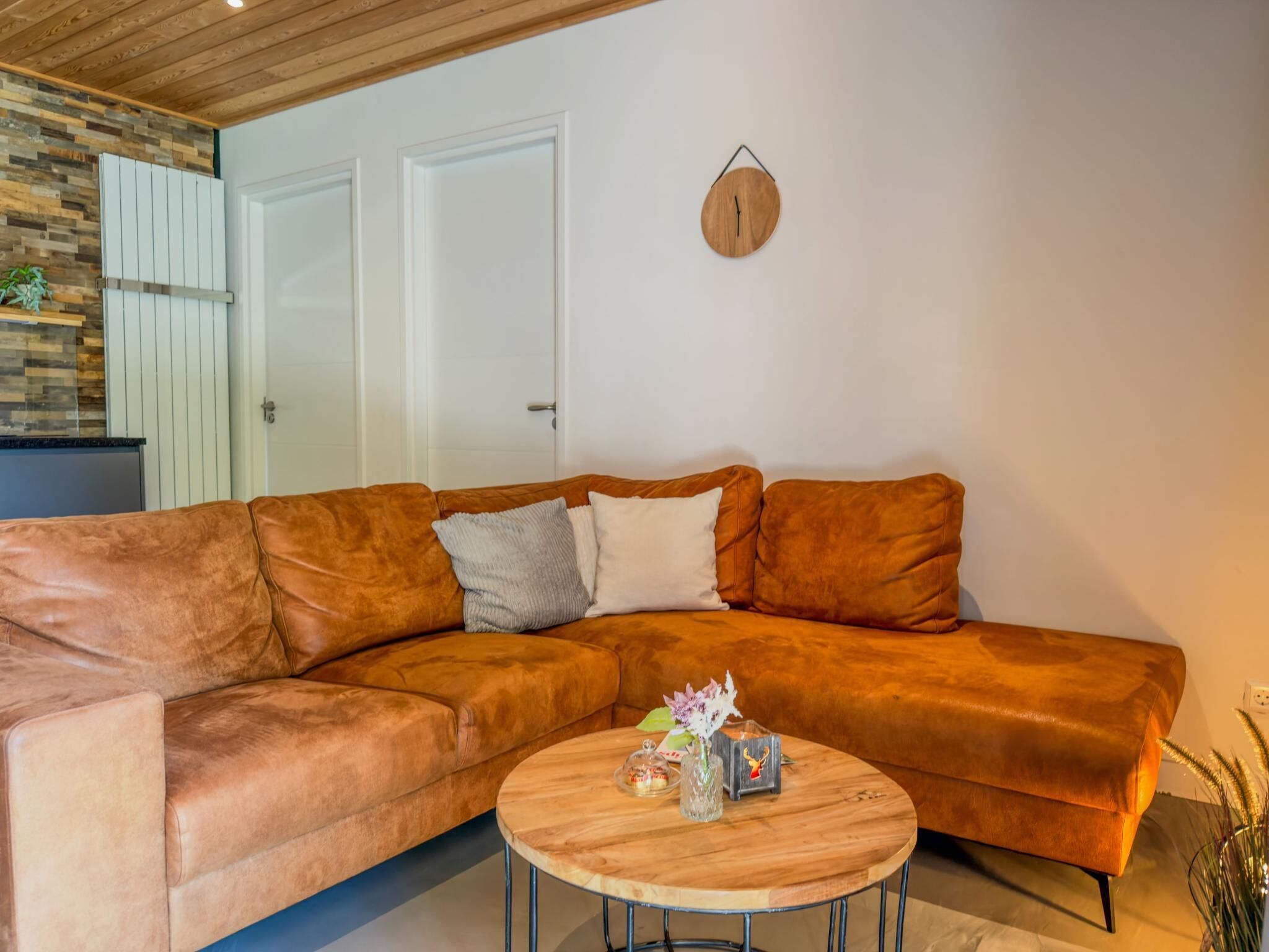 A living room with a brown leather sofa, a round wooden coffee table, and a wall-mounted clock.