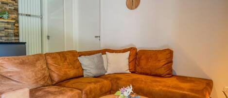 A living room with a brown leather sofa, a round wooden coffee table, and a wall-mounted clock.