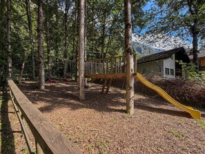 A playground with a slide and swings surrounded by trees.