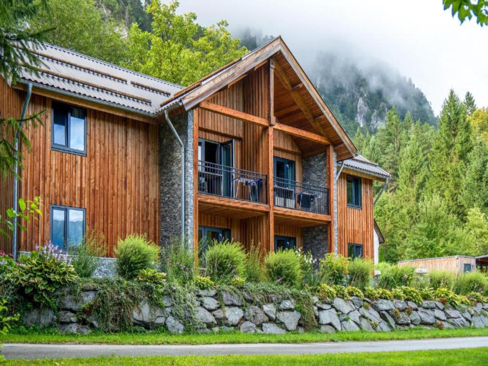 A wooden chalet with a stone foundation, multiple balconies, and a lush garden.