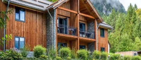 A wooden chalet with a stone foundation, multiple balconies, and a lush garden.