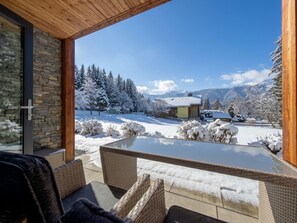 Ein moderner Sitzbereich im Freien mit einem Tisch aus Glas und Korbstühlen, mit Blick auf eine verschneite Landschaft aus Bäumen und Bergen.